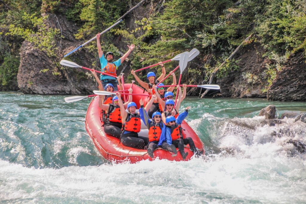 A red raft of smiling and stoked adults about to hit a big rapid on the Kananaskis River
