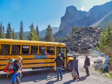 People standing outside a yellow bus to takes them home after an adventure at the foot of the rock pile at Moraine Lake in Banff National Park