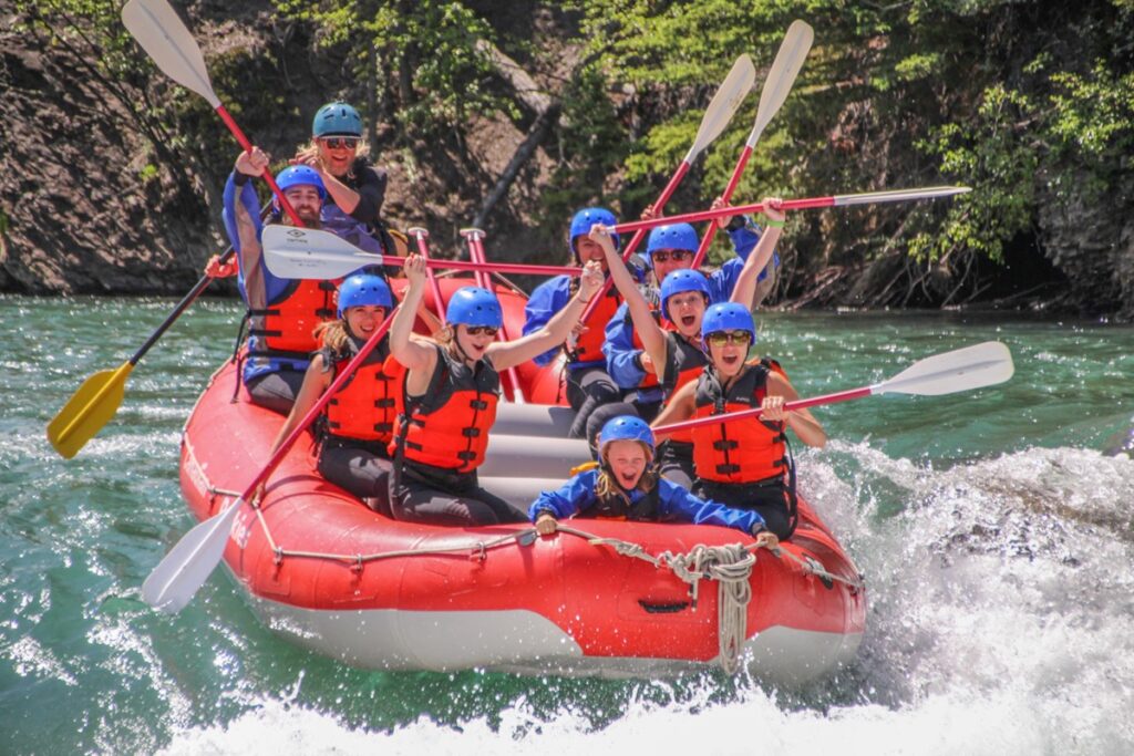 Group of people having lots of fun; smiling and shouting joy as they go into the rapid in a red raft with Canadian Rockies Rafting