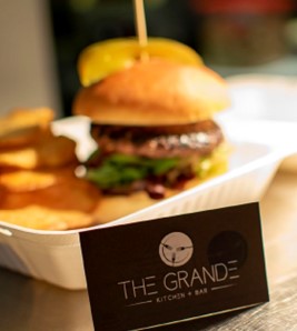 The Grande Kitchen and Bar in Canmore, Alberta showcasing a beef burger with a side of chips, their Tuesday dining special