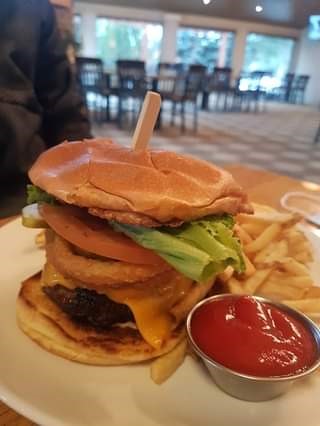 A towering beef burger with all the fixings; cheese, tomato, lettuce, onion rings, with a side of ketchup and fries.  The dining special at Sandtraps in Canmore, Alberta