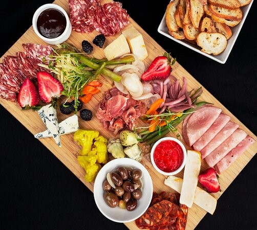 A charcuterie board; displaying meats, cheeses, fruit, vegetables, olives and crackers.  
