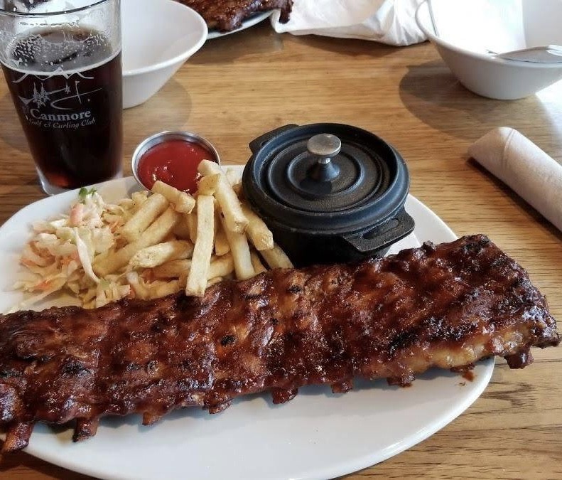 Plate of a rack of ribs with a side of fries and coleslaw served with a fresh pints of beer in Canmore, Alberta