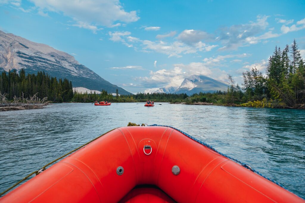 Red raft floating down the river surrounded by forest and the Rocky Mountains