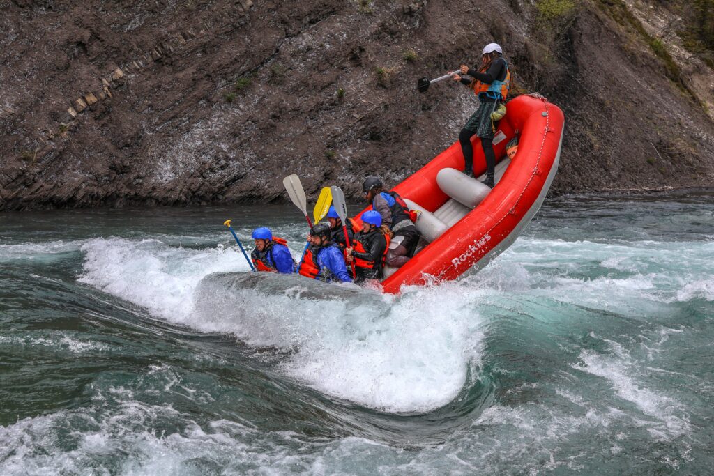 Rafters in red raft surfing a wave on the Kananaskis Surf Trip with Canadian Rockies Rafting
