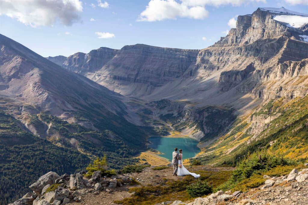 Bride and Groom stand atop of a mountain ridge overlooking a turquoise lake in the Canadian Rocky Mountains captured by Wild Alpine Image Co. - an epic location to host bachelor and bachelorette weekends explored on Canadian Rockies Rafting tours.